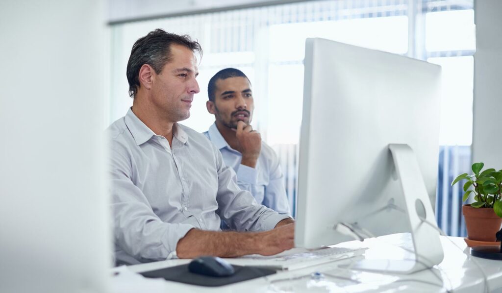 2 Männer sitzen zusammen am Computer und lösen IT Probleme.